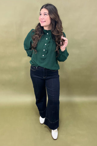 Woman wearing a green blouse and black jeans against a beige background