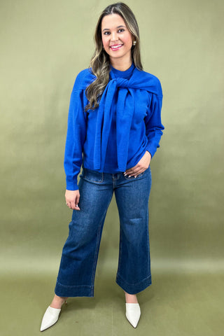 Woman wearing a blue blouse with a large bow and blue jeans on a green background