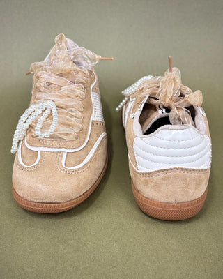 Pair of beige sneakers with decorative laces on a green background