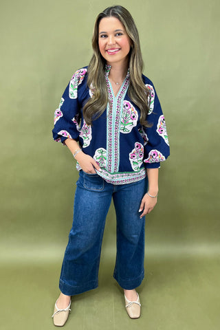 Woman wearing a navy blue blouse with colorful floral patterns on a green background