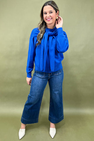 Woman wearing a blue blouse and jeans against a green background