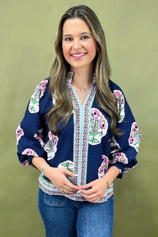 Woman wearing a blue embroidered top against a green background