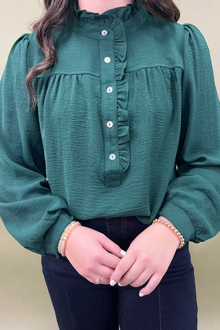 Green blouse with ruffled collar and long sleeves worn by a person against a beige background