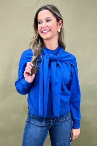 Woman wearing a blue blouse with a large bow tie against a beige background