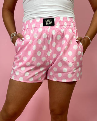 Person wearing pink polka dot shorts with a visible brand label on a pink background