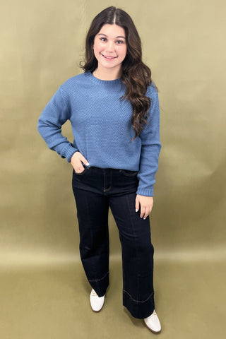 Woman wearing a blue sweater and black pants against a beige background