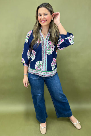 Woman wearing a navy blue embroidered top and jeans on a green background
