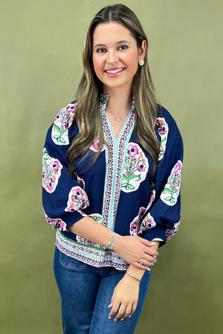 Woman wearing a navy blue blouse with colorful floral patterns on a green background