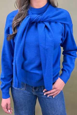 Person wearing a blue sweater with a large bow detail on a plain background