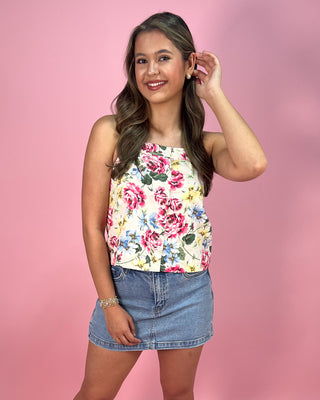 Woman wearing a floral top and denim skirt against a pink background