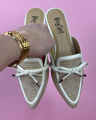 White loafers with a bow detail worn by a person on a pink background