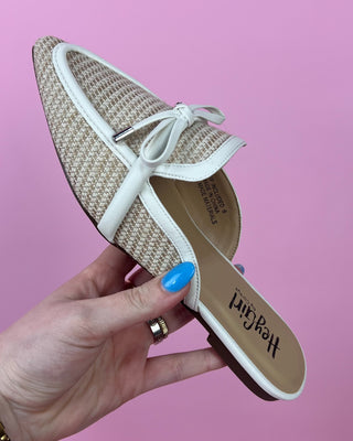 Hand holding a woven shoe with a white bow against a pink background