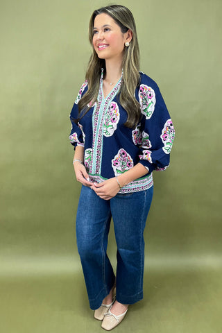 Woman wearing a navy blue embroidered top and jeans on a green background