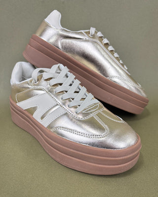 gold sneakers with brown sole held by a hand against a green background