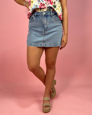 Person wearing a floral top and denim skirt on a pink background