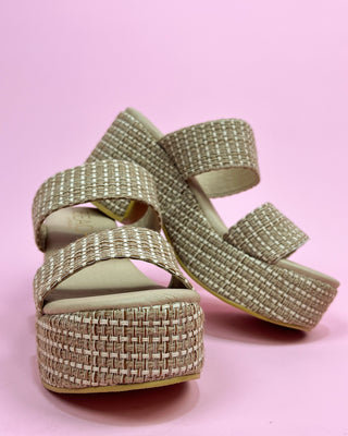 Gold platform sandals with woven design on a pink background