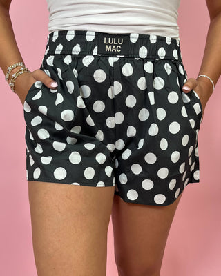 Black polka dot shorts with 'LULU MAC' branding on a pink background