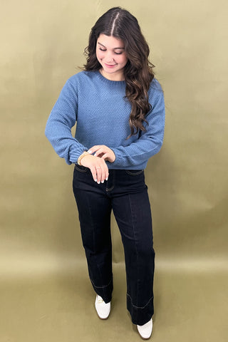 Woman wearing a blue sweater and black jeans against a beige background