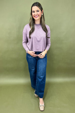 Woman wearing a purple sweater and blue jeans against a green background