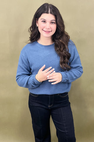 Woman wearing a blue sweater and dark jeans against a beige background