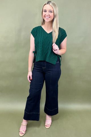 Woman wearing a green knitted top and black pants against a green background
