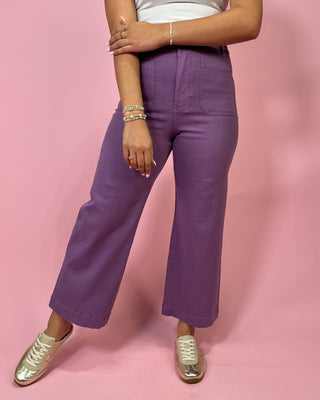 Person wearing purple pants and gold shoes on a pink background