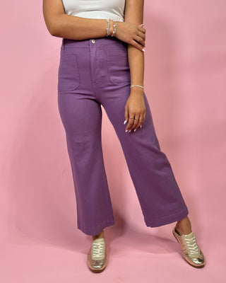 Person wearing purple pants and white top on a pink background