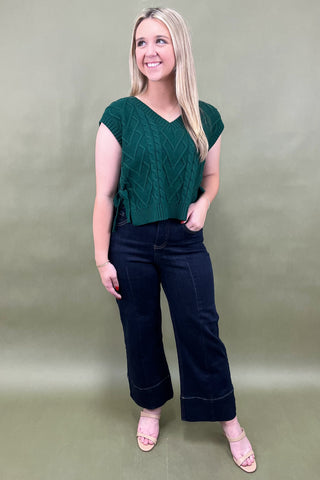 Woman wearing a green top and black pants against a plain background