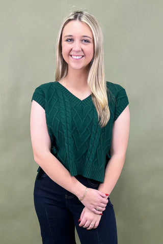 Woman wearing a green cable knit top against a plain background