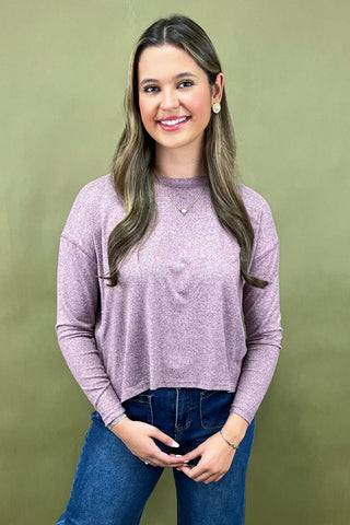 Woman wearing a purple sweater and blue jeans against a green background