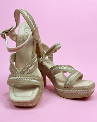 Beige high-heeled sandals with braided details on a pink background