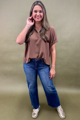 Woman wearing a brown shirt and blue jeans against a green background