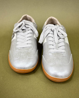 Pair of silver sneakers with tan soles on a beige background