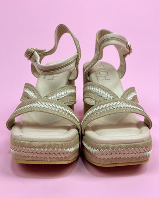 Beige sandals with braided details on a pink background