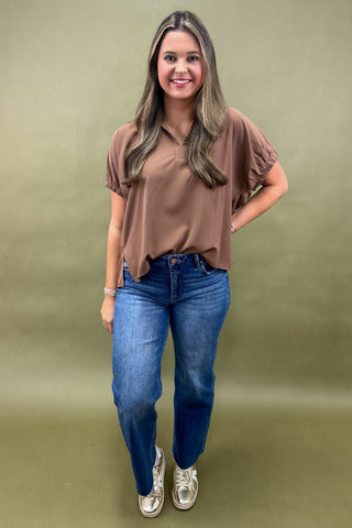 Woman wearing a brown blouse and blue jeans against a green background