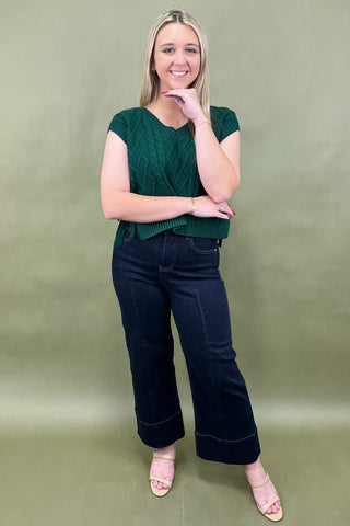 Woman wearing a green top and dark blue jeans against a green background