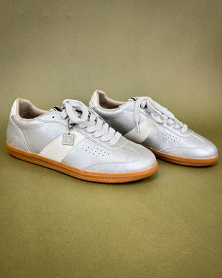 Pair of silver sneakers with tan soles on a beige background