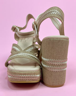 Beige wedge sandals with braided details on a pink background
