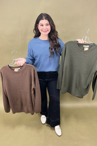 Woman holding two sweaters, one brown and one green, against a beige background