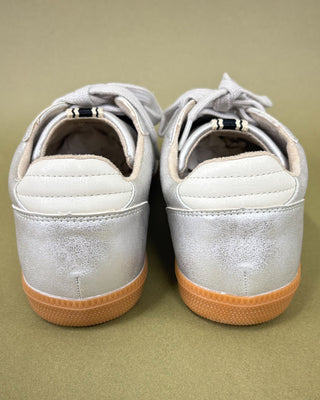 Pair of silver sneakers with tan soles on a beige background
