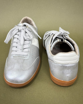 Pair of silver sneakers with brown soles on a green background