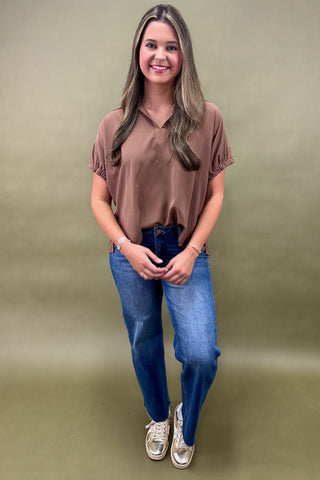Woman wearing a brown blouse and blue jeans against a green background