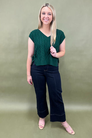 Woman wearing a green top and black pants against a plain background