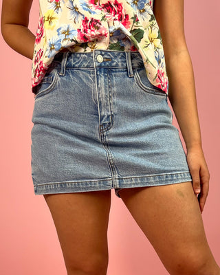 Person wearing a floral top and denim skirt on a pink background