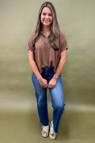 Woman wearing a brown shirt and blue jeans against a green background