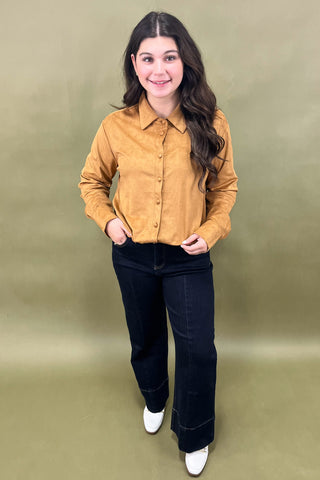 Woman wearing a mustard yellow shirt and black pants against a green background