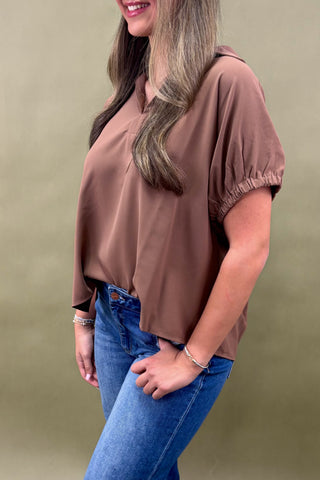 Woman wearing a brown top and blue jeans against a beige background
