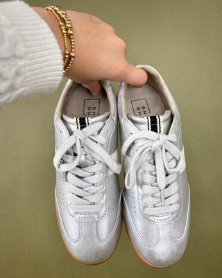 silver sneakers held by a hand against a plain background