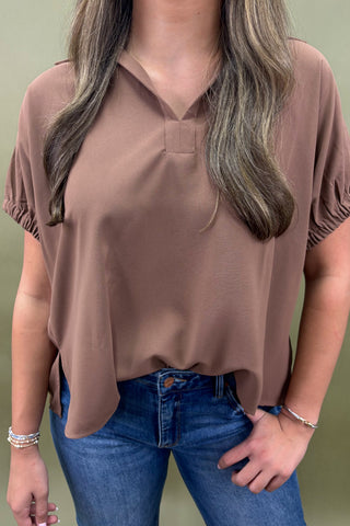 Woman wearing a brown blouse and blue jeans against a plain background
