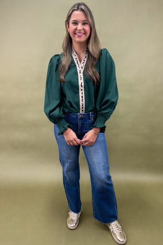 Woman wearing a green blouse with lace details and blue jeans against a beige background